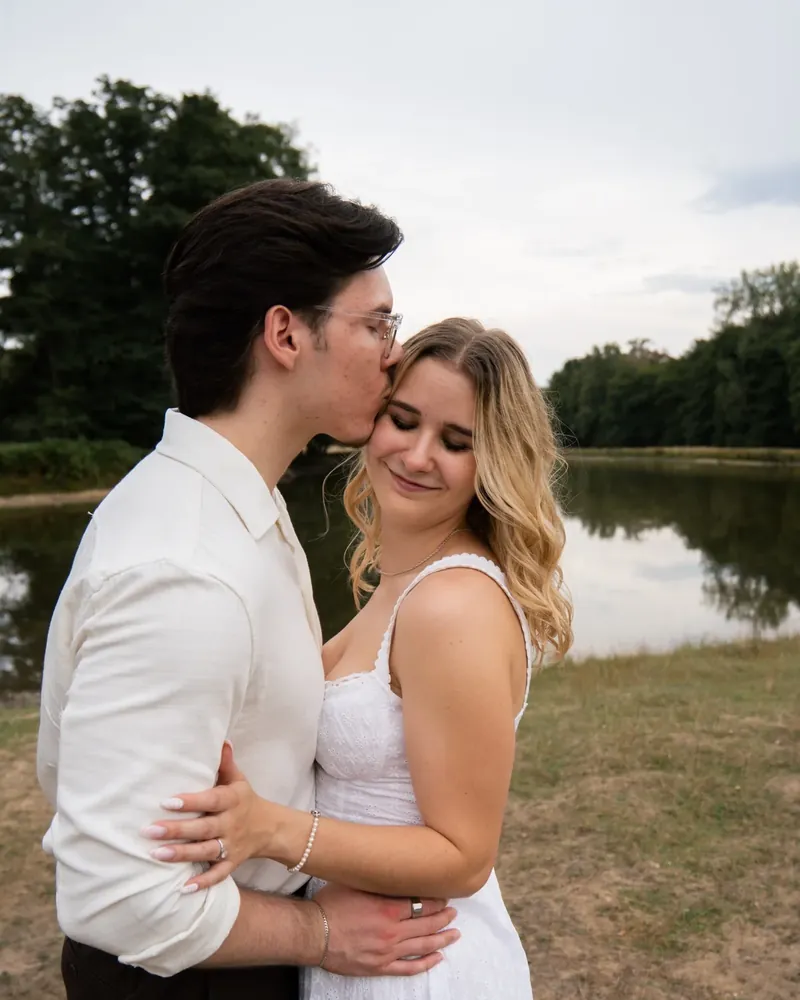 Couple shoot at Wildpark Dülmen: he kisses her forehead, both standing by the water